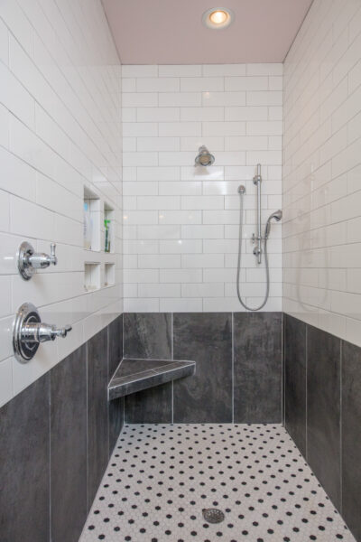 View of the shower. Triangle seat in the shower. White and black tile.